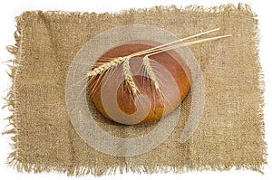 Wheat rye bread and three wheat spikes on a sackcloth
