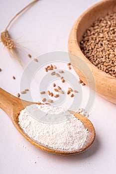 Wheat seeds grains in wooden bowl near with flour in spoon spatula with heap of grains and with ear of wheat, angle view