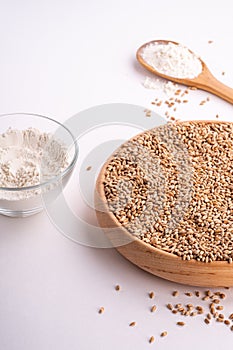 Wheat seeds grains in wooden bowl, wheat flour in glass bowl, near with flour in spoon spatula with heap of grains, angle view