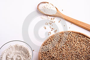 Wheat seeds grains in wooden bowl, wheat flour in glass bowl, near with flour in spoon spatula with heap of grains, angle view