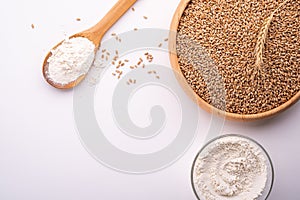 Wheat seeds grains in wooden bowl, wheat flour in glass bowl, near with flour in spoon spatula with heap of grains, ear of wheat