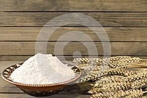 Wheat spikelets and flour on wooden plank background