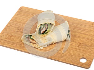 Wheat tortilla roll with chicken breast lettuce and spices on a cutting board.