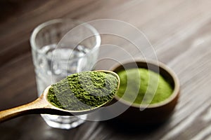 Wheatgrass or barley grass powder in spoon and glass of water. Detox juice preparation