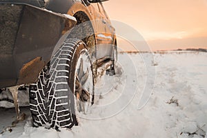 The wheel is buried in the snow. The car goes on a winter field.