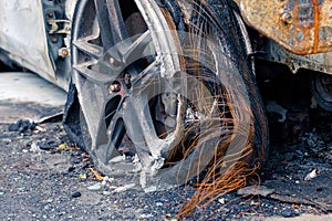 Wheel of burned car. Burnt flat tire on the car is on the gray asphalt road to illustrate an article about a fire, banditry, an