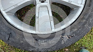 A wheel from a car with a damaged tire, worn out due to prolonged use, numerous damage.