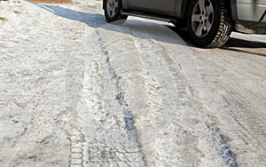 The wheel of the car on slippery winter road. Studded rubber on ice. Dangerous driving conditions. Icy road with traces of car