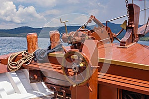 A wheel and deck of a wooden old sailing yacht against the background of the sea and the blue sky