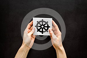 Wheel of dharma - Buddhist religion symbol - in hands on black table top view