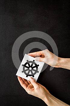 Wheel of dharma - Buddhist religion symbol - in hands on black table top view copy space