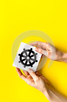 Wheel of dharma - Buddhist religion symbol - in hands on yellow table top view copy space