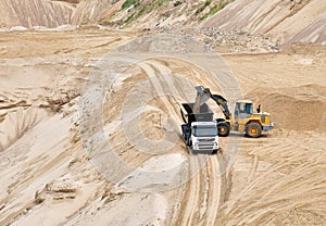 Wheel front-end loader loading sand into heavy dump truck at the opencast mining quarry. Dump truck transports sand in open pit