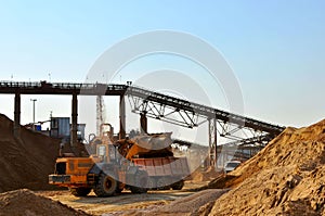 Wheel front-end loader unloading sand into heavy dump truck. Crushing factory, machines and equipment for crushing, grinding stone