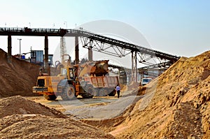 Wheel front-end loader unloading sand into heavy dump truck. Crushing factory, machines and equipment for crushing, grinding stone