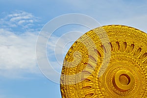 The Wheel of Life and Buddhist Stories is a golden yellow sculpture with Asian Buddhist motifs against a beautiful blue sky