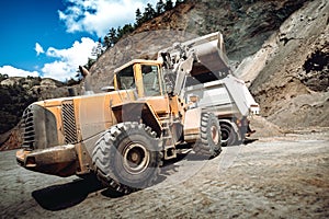 Wheel loader bulldozer with backhoe loading dumper trucks on construction site