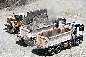 Wheel loader bulldozer loading two dumper trucks in sandpit at highway construction