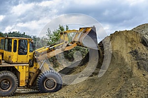 Wheel loader Excavator with backhoe unloading sand at eathmoving works in construction site quarry