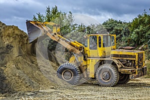 Wheel loader Excavator with backhoe unloading sand at eathmoving works in construction site quarry
