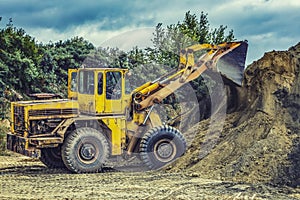 Wheel loader Excavator with backhoe unloading sand at eathmoving works in construction site quarry