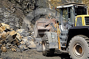 A wheel loader / front loader machine working on a heap of stones with its shovel at a quarry