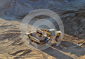 Wheel loader loads sand into heavy mining dump truck at the opencast mining quarry