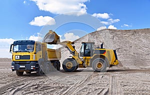 Wheel loader loads a truck with sand in a gravel pit