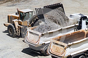wheel loader working on construction site and loading gravel on dumper trucks