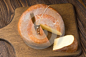 Cheese wheel and slice on a cutting board over a wooden table on
