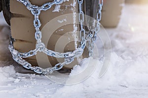 Wheel in the snow with safety and anti-skid chains. Loader or tractor with chains on wheels close-up. Driving safety in