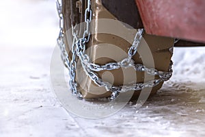 Wheel in the snow with safety and anti-skid chains. Loader or tractor with chains on wheels close-up. Driving safety in