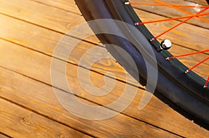 The wheel of a stylish bicycle with a black rim and a black rubber tire, red spokes, a stylish wooden background.