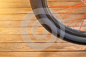 The wheel of a stylish bicycle with a black rim and a black rubber tire, red spokes, a stylish wooden background.