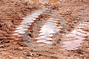 Wheel trace on road, puddle and mud after rain. Traces on soil of tractor, excavator, car, automotive tire tracks on muddy trail.