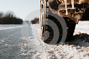 Wheel winter studded tires of car standing on snowy road during day, copy space. Close-up, low angle view