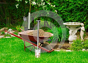 Wheelbarrow Full of Dirt with Leaning Shovel in Garden