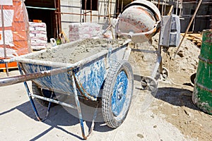 Wheelbarrow with mortar and empty cement mixer machine were placed on construction site