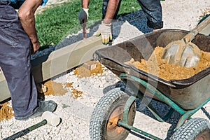 Wheelbarrow with sand and workers hands on construction site