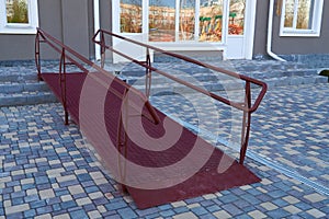 Wheelchair access ramp for entrance of residential multistory building, city street and tiles sidewalk