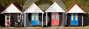 Wheelchair and colourful beach huts with blue and red doors in a row traditional English structure panorama