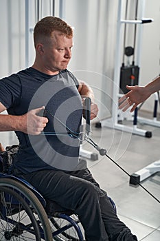 Wheelchair young man pulls on weight trainer at rehabilitation clinic photo