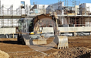 Wheeled excavator in front of modern white building under construction