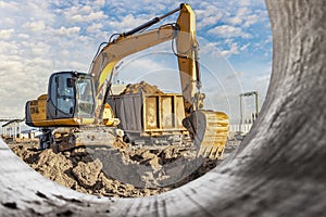 A wheeled excavator loads a dump truck with soil and sand. An excavator with a high-raised bucket against a cloudy sky View from