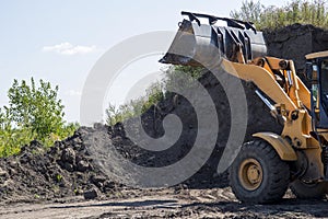 Wheeled tractor with bucket clears the soil layer for subsequent construction