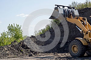 Wheeled tractor with bucket clears the soil layer for subsequent construction