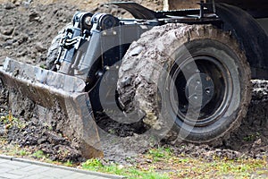 Wheeled tractor with shovel clears ground on cloudy rainy day. Dirty bulldozer shovel close-up.