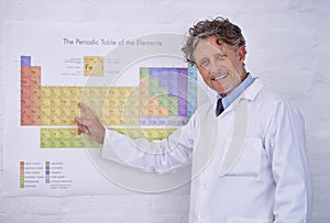 Where it all begins. A cropped portrait of a mature scientist pointing to the periodic table of elements.