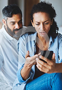 Where did all our money go. a dismayed couple receiving bad news via a smartphone at home.