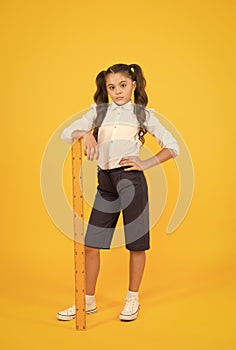 Where student comes first. Serious small student holding wooden ruler on yellow background. Little student learning